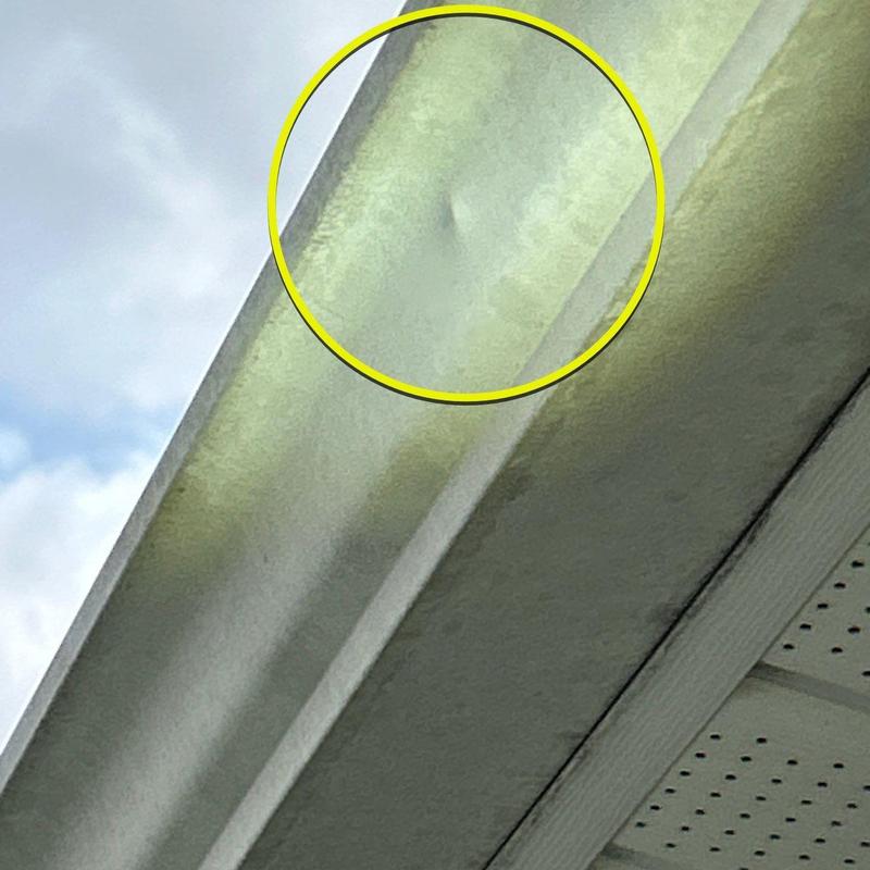 Metal gutter dent with hail damage highlighted in yellow circle