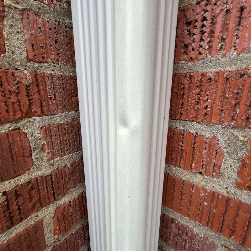 Downspout with dent against brick wall