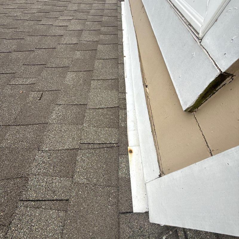 Asphalt roof shingles near dormer flashing showing damage