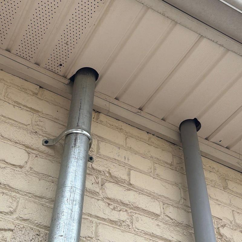 Metal downspouts with soffit vent and brick wall
