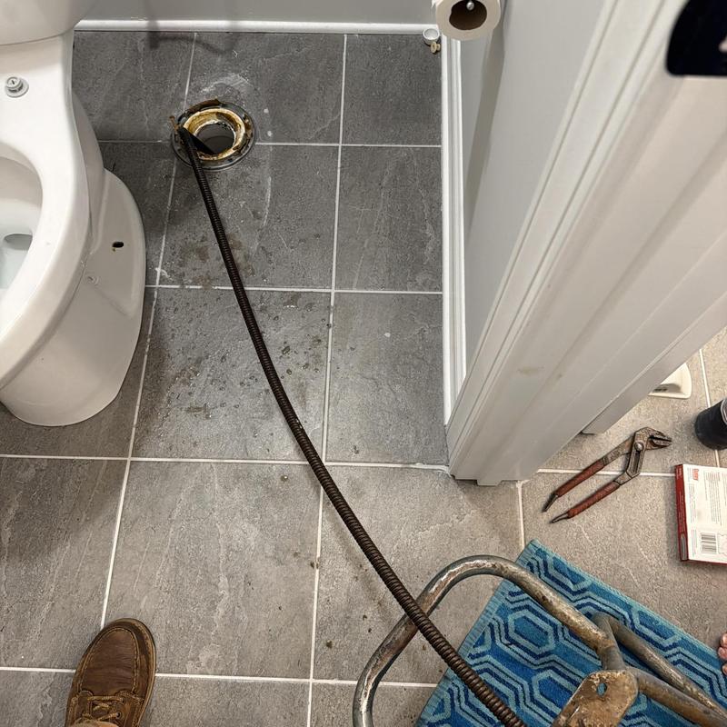 Toilet flange with plumbing snake tool in bathroom Toilet flange with plumbing snake tool in bathroom
