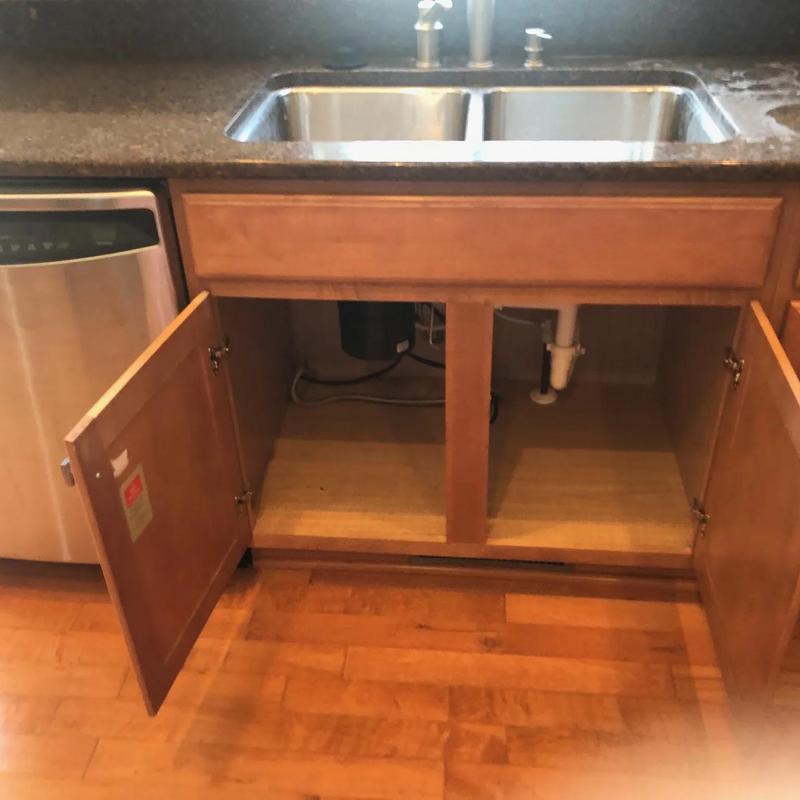 Kitchen sink cabinet with open doors and visible plumbing Kitchen sink cabinet with open doors and visible plumbing