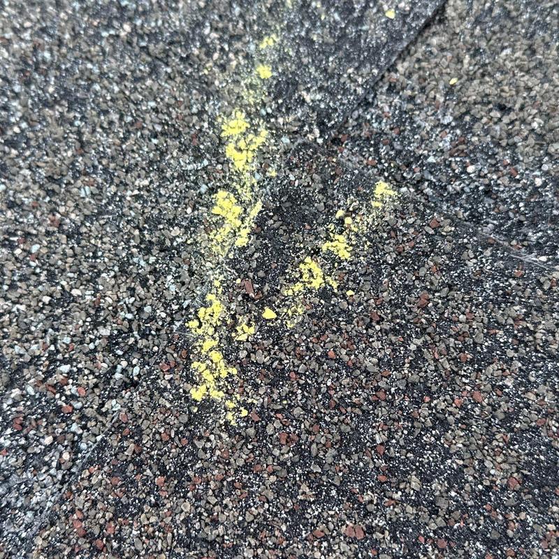 Roof shingle damage marked with yellow chalk on asphalt shingles