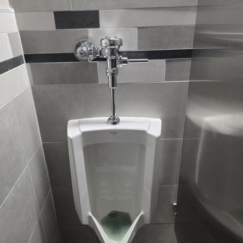 Sloan flush valve on white urinal with tiled wall Sloan flush valve on white urinal with tiled wall