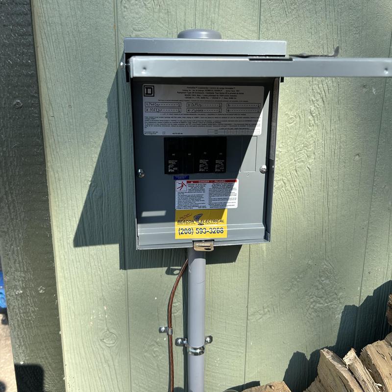 Electrical breaker panel box with open door on green siding