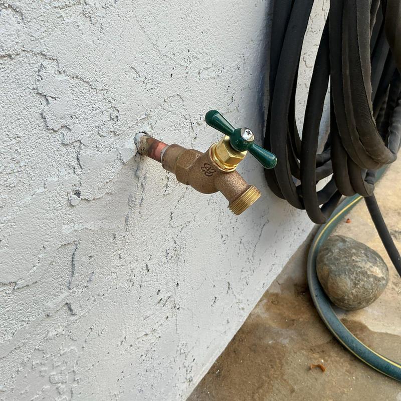 Exterior 12 hose bib with green handle and garden hose