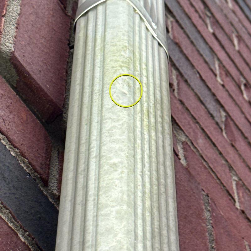 Metal downspout with dent damage on brick wall