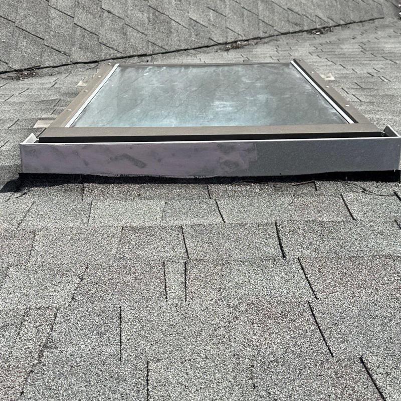 Roof skylight flashing and shingle inspection on gray roof