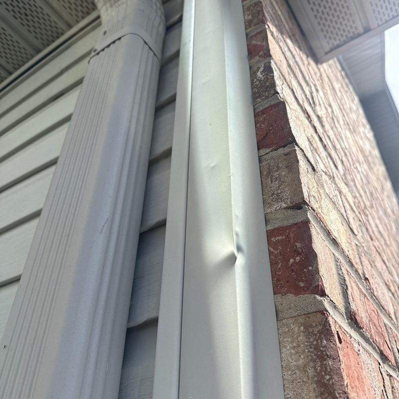 Metal flashing dent on house exterior near brick wall
