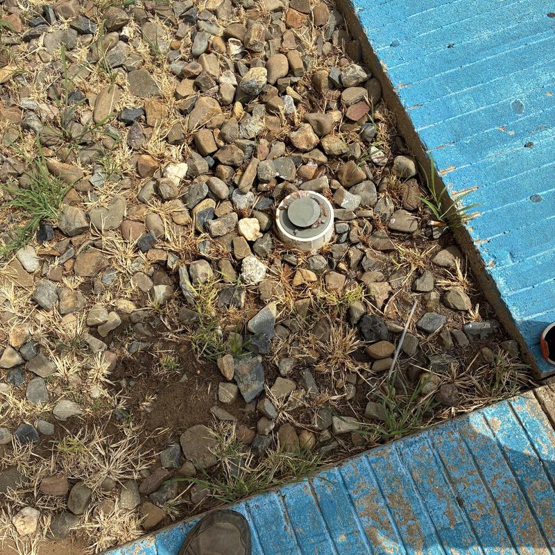 Outdoor cleanout cap amidst gravel and blue curb