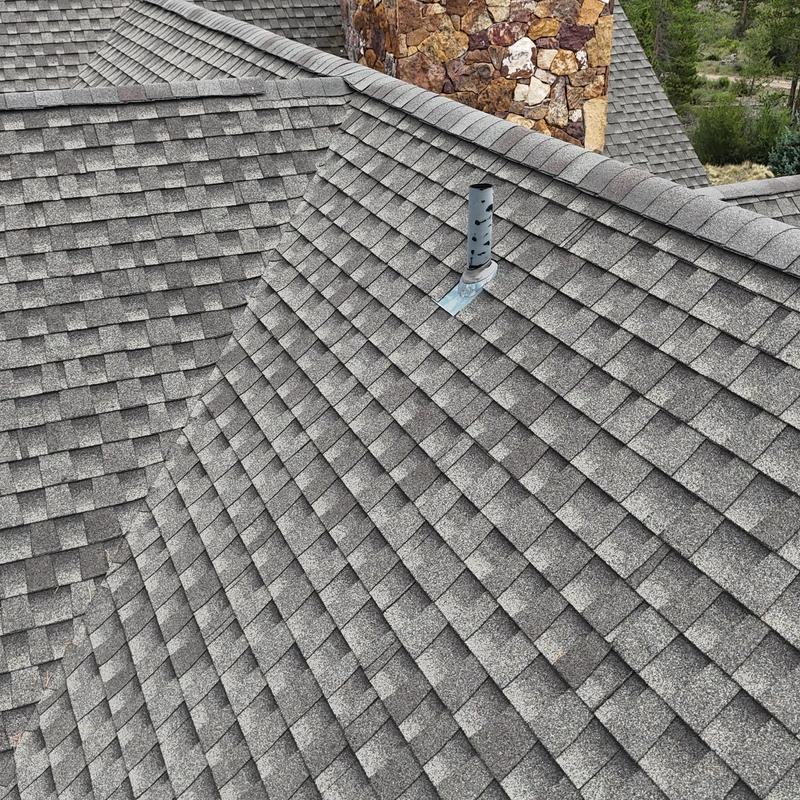 Asphalt shingle roof with vent pipe near stone chimney
