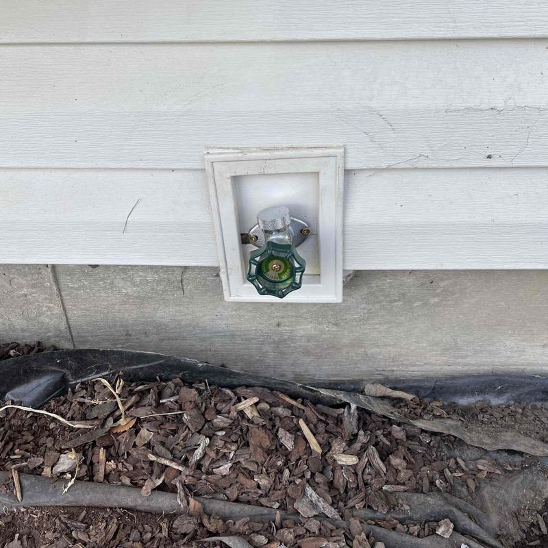 Hose bib with green handle on house exterior wall