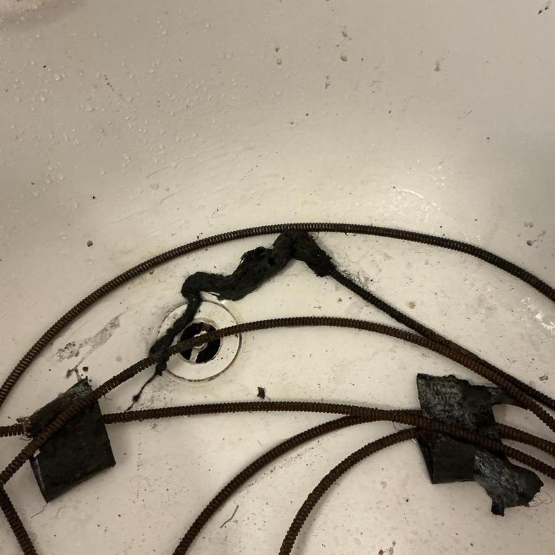 Bathtub overflow drain with clogged hair and cleaning cable Bathtub overflow drain with clogged hair and cleaning cable
