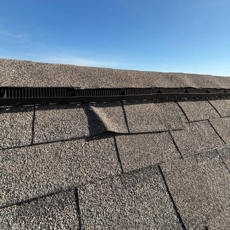Roof shingles lifted from hail damage near ridge vent