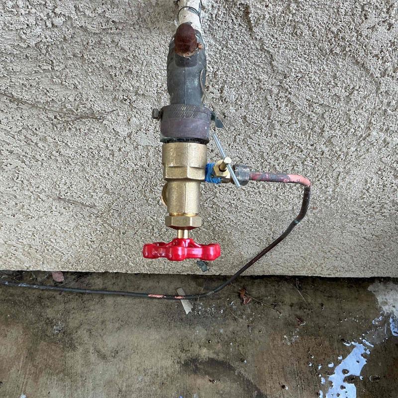 Hose bib with saddle valve and red handle installed outdoors