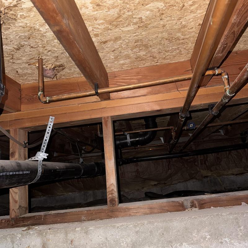 Copper water piping and black drain pipes in crawlspace