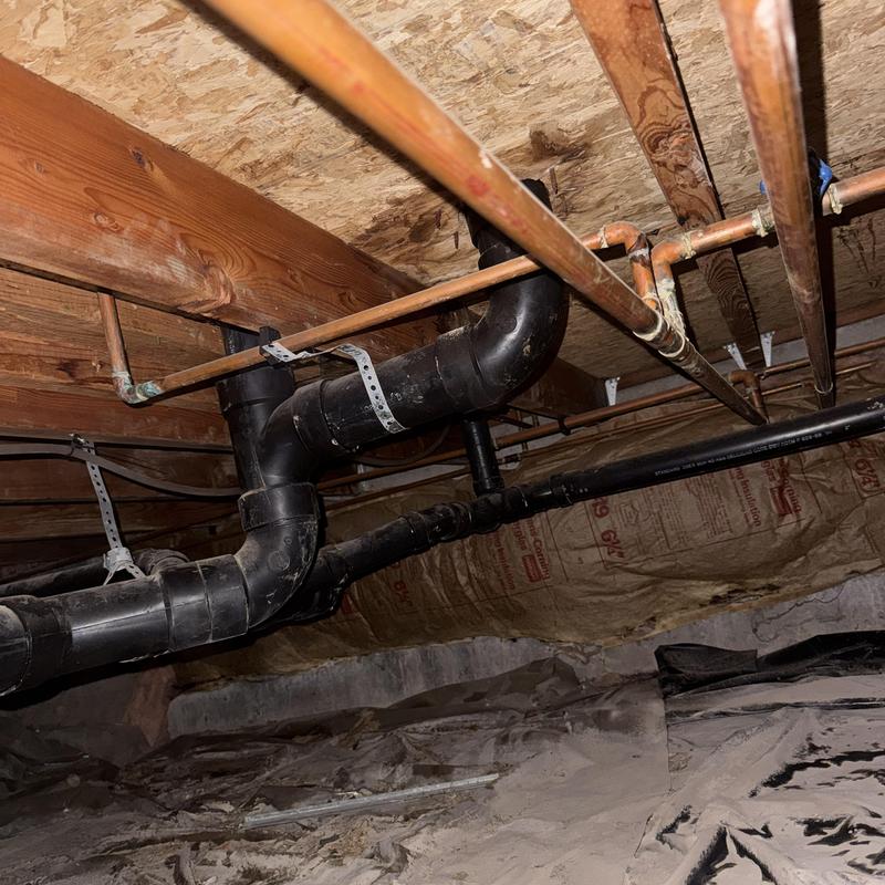 Copper piping and black drain pipes in crawl space