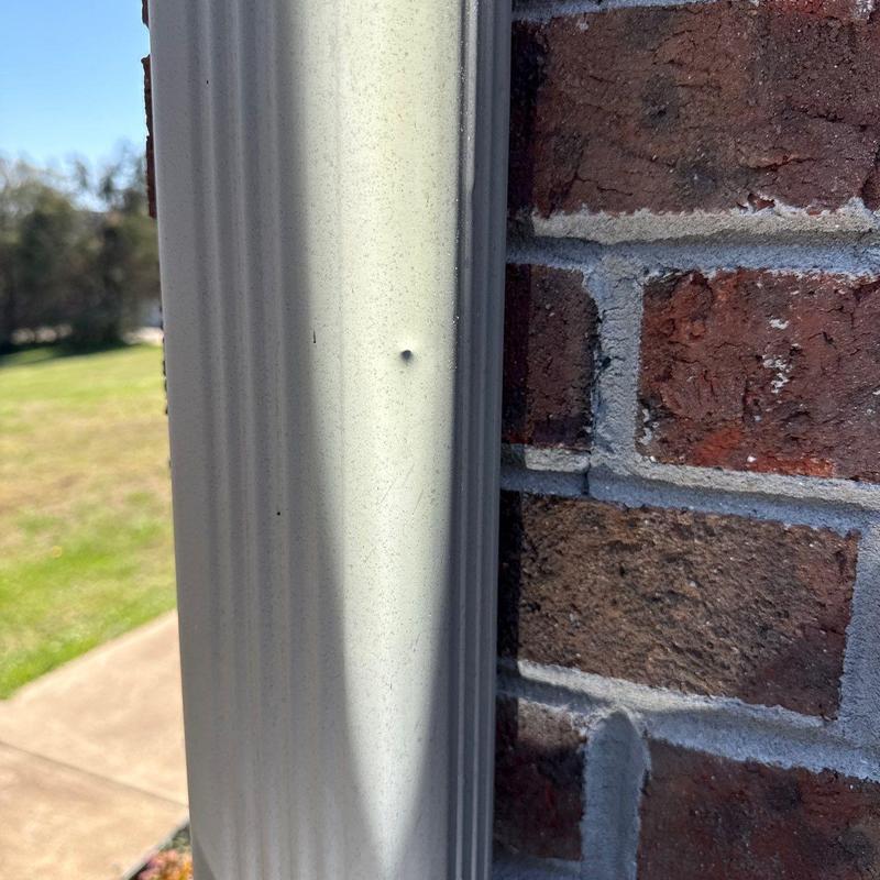 Metal downspout dent on exterior brick wall