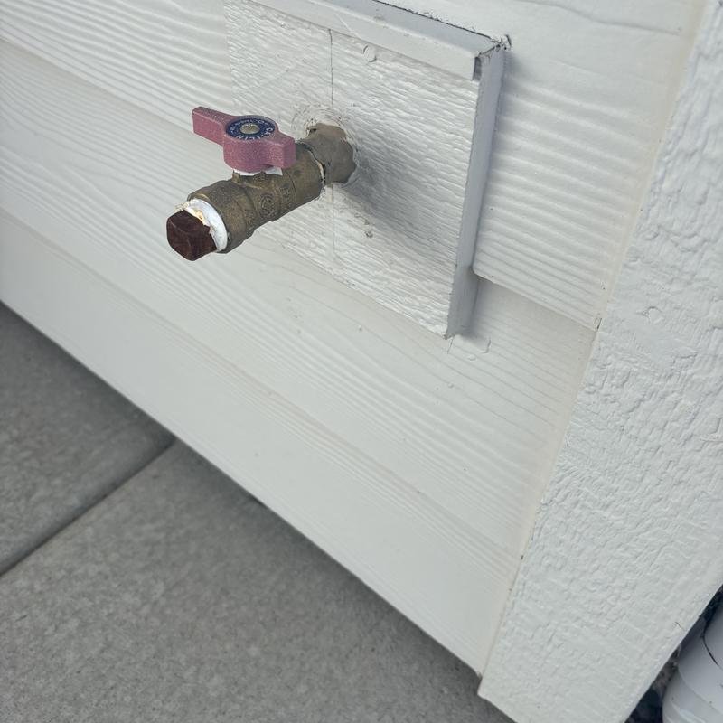Outdoor water spigot with pink valve handle on siding