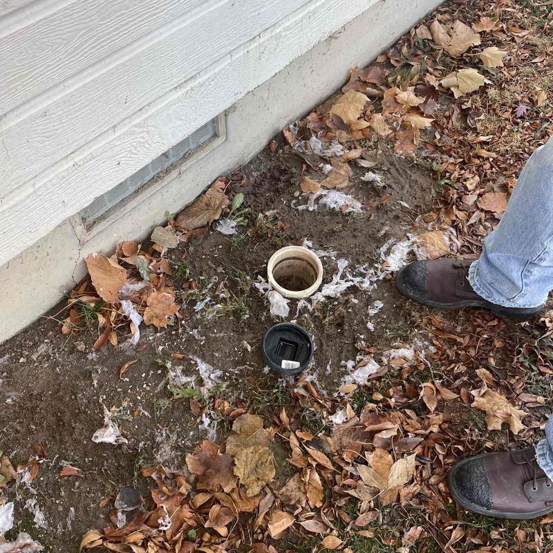Sewer cleanout exposed for inspection near house foundation