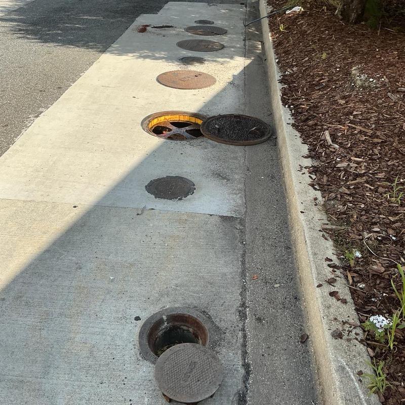 Sewer line with multiple opened manhole covers on sidewalk Sewer line with multiple opened manhole covers on sidewalk