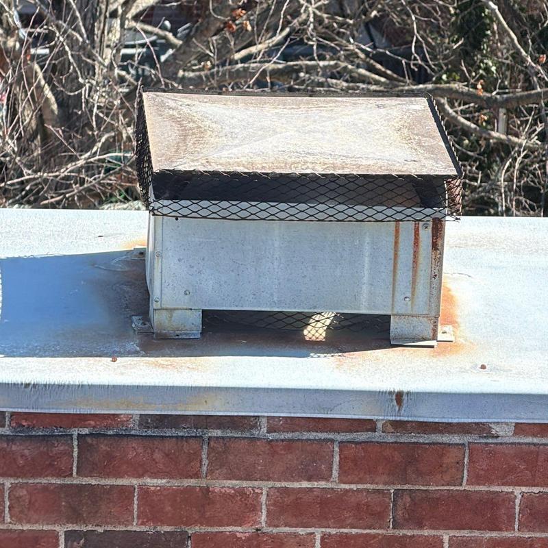 Metal roof vent with rust stains on brick chimney top