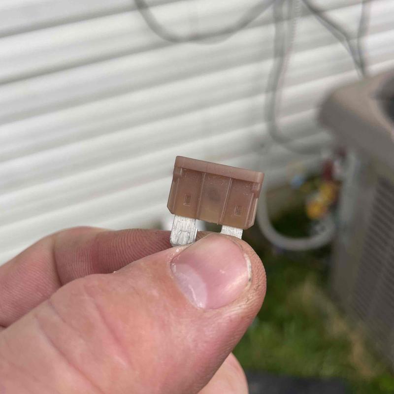 Low voltage fuse held in technician's hand near AC unit