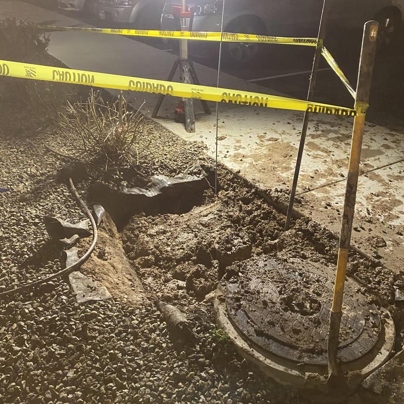 Water meter vault excavation with caution tape at night