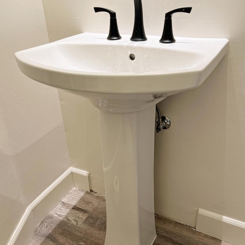 Pedestal sink with black faucet and water lines