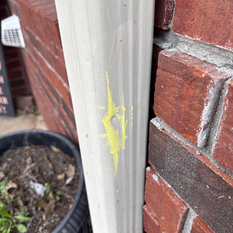 Downspout with yellow paint mark on brick wall