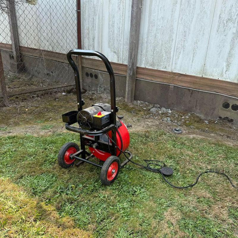 Drain cleaning machine with cable on grass near building