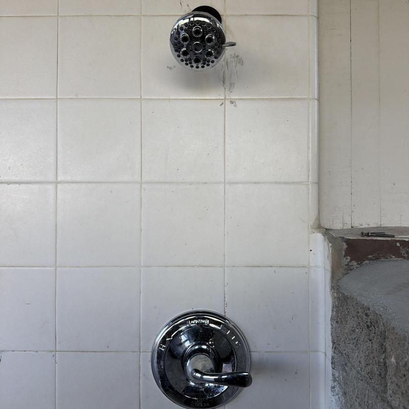 Shower valve and chrome trim kit on white tile wall