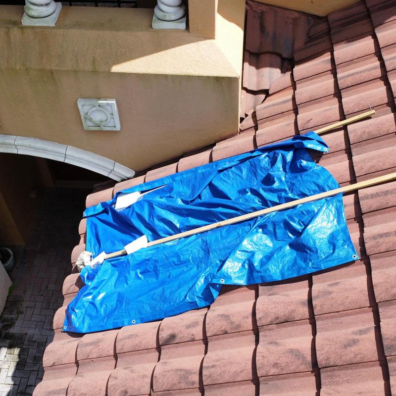 Roof vent covered with blue tarp on tile roof
