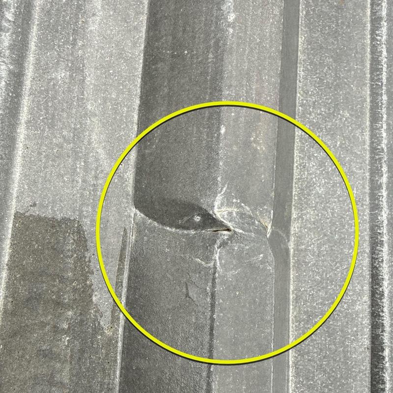 Metal roofing panel with hail damage dent and crack