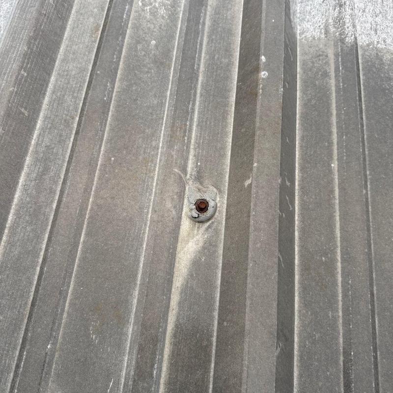 Metal roofing panel with hail impact damage and rusted screw