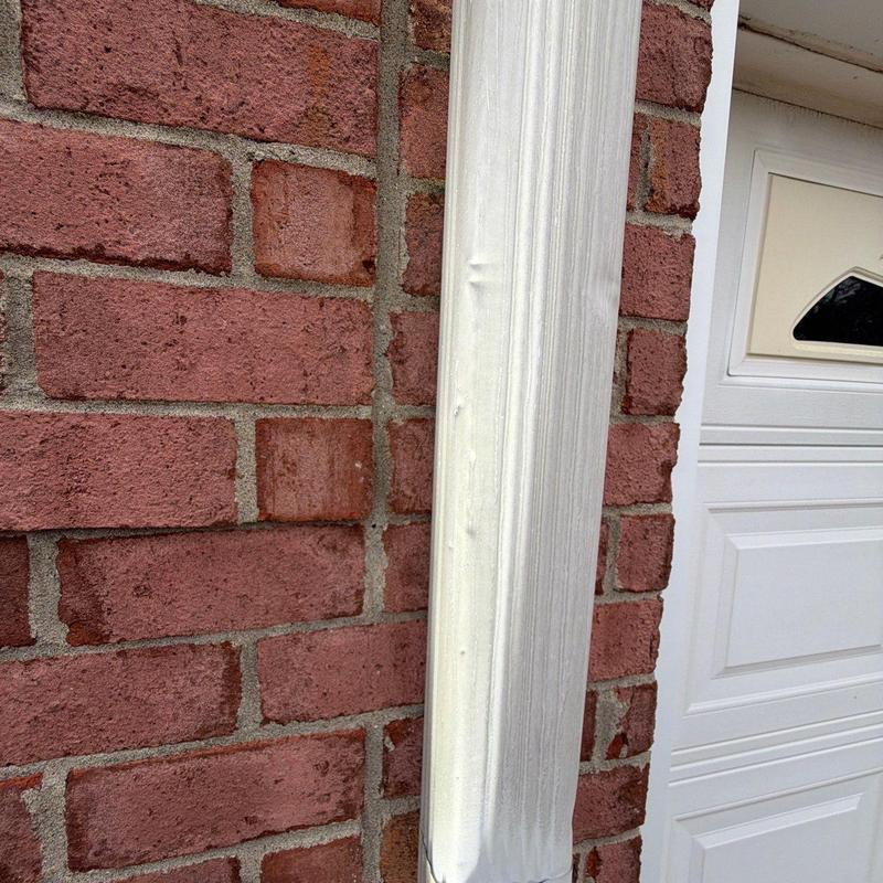 Downspout dent damage on brick exterior near garage door