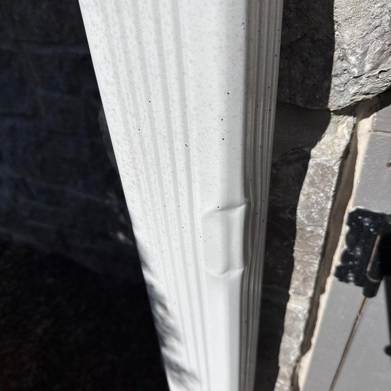 Metal downspout dented from hail impact near brick wall