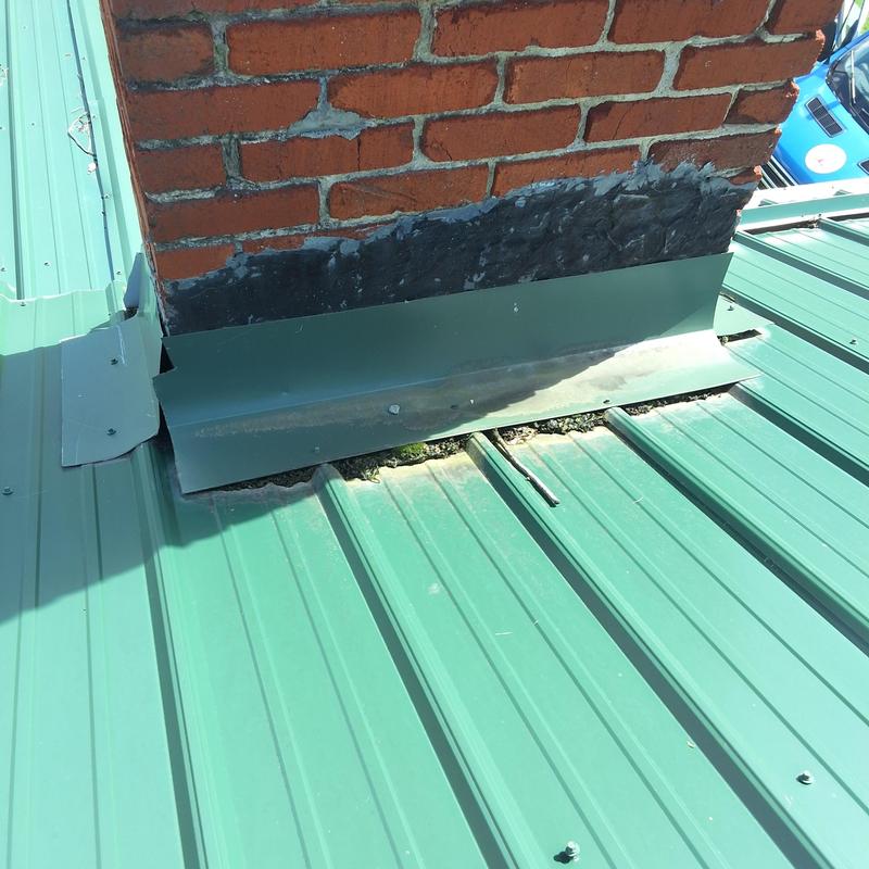 Chimney flashing on green metal roof near leak source