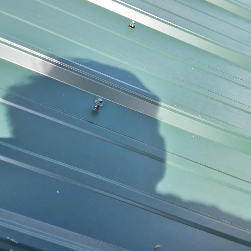 Metal roof panels with exposed fasteners near chimney shadow