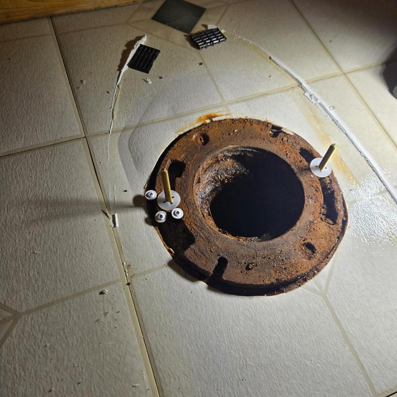 Rusty toilet flange with screws on tiled floor