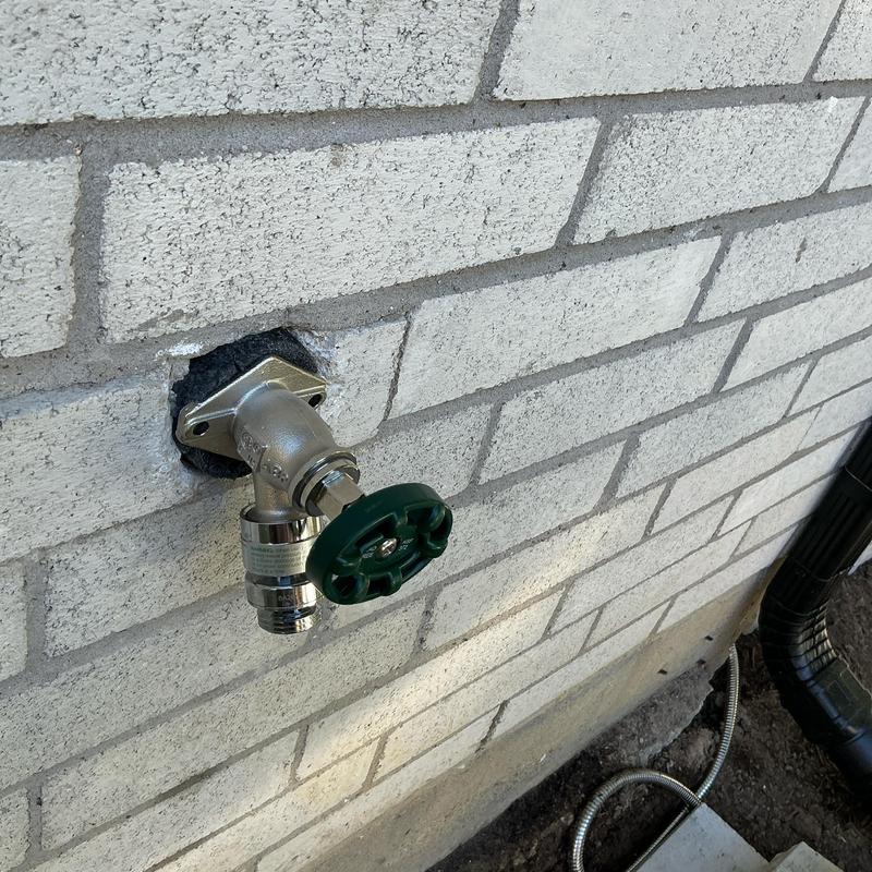 Frost proof outdoor faucet with green handle on brick wall
