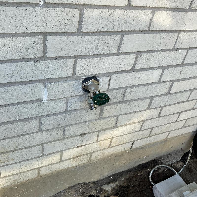 Frost proof outdoor faucet with green handle on brick wall