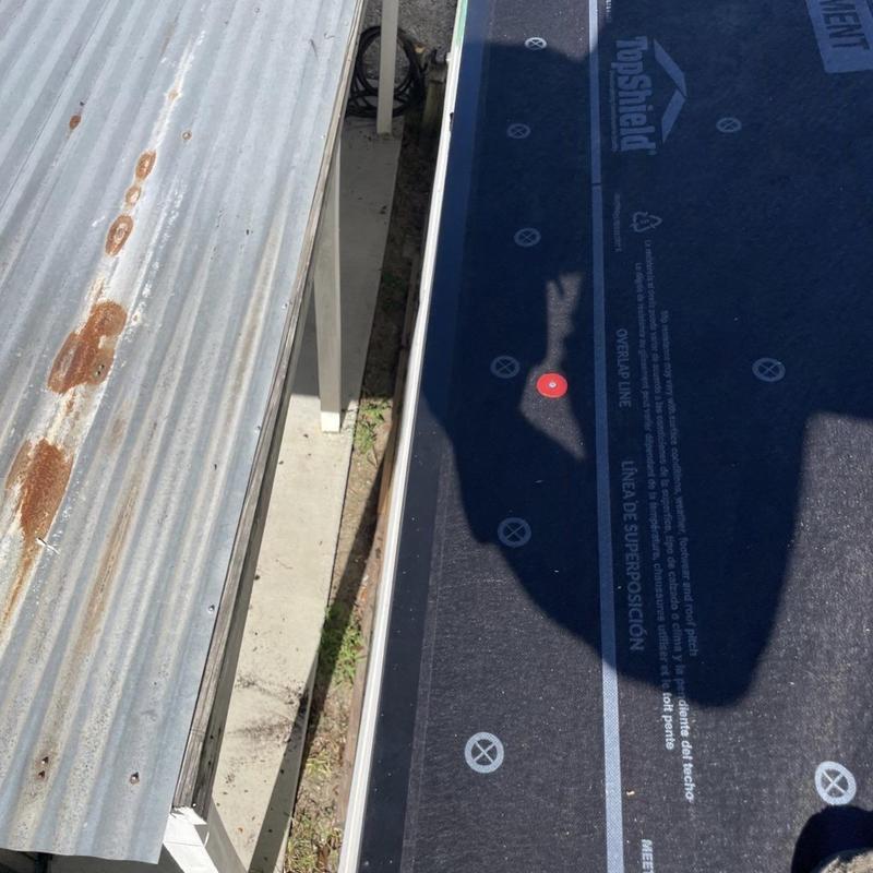 Synthetic roofing underlayment installation with metal roof nearby