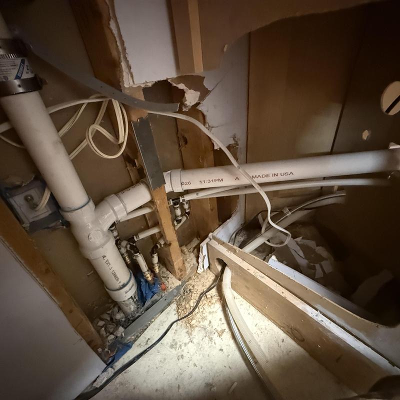 PVC drain and water line installation behind drywall panel