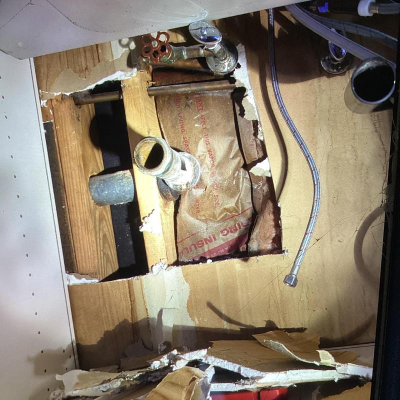 Kitchen sink plumbing with exposed pipes and drywall cutout
