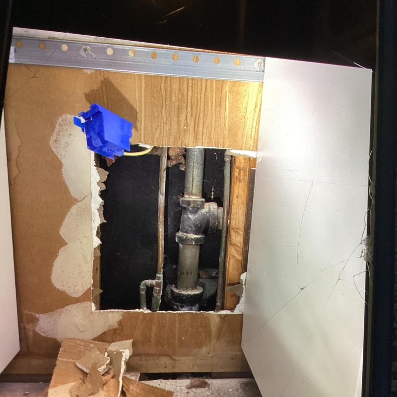 Cast iron drain pipe exposed behind drywall cutout