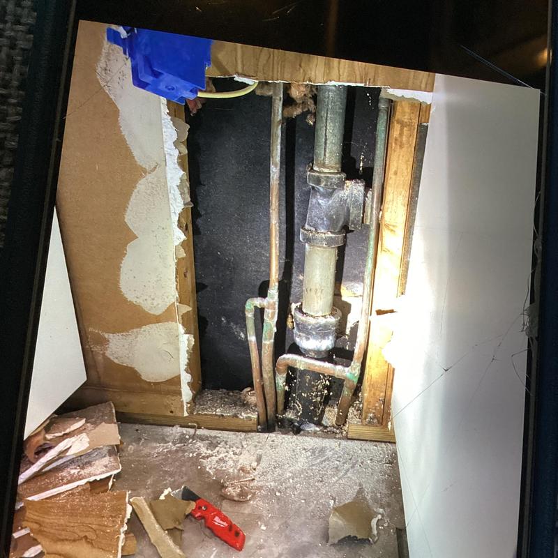 Cast iron drain pipe and copper water lines exposed behind wall