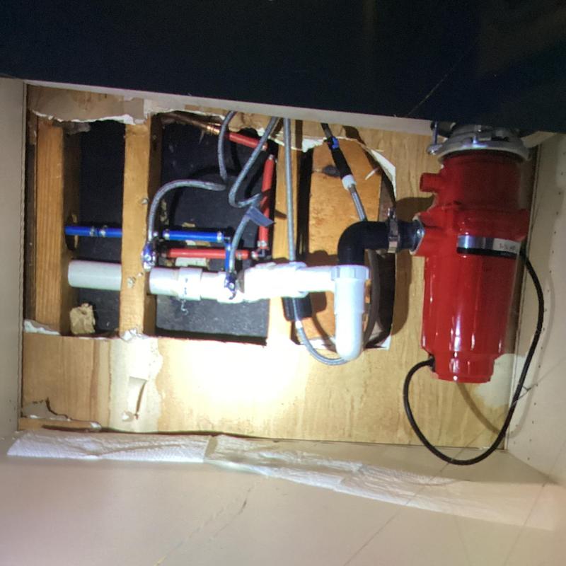 Kitchen sink drain and disposal plumbing exposed under cabinet