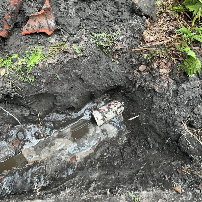 Clay sewer pipe exposed in muddy trench outdoors Clay sewer pipe exposed in muddy trench outdoors