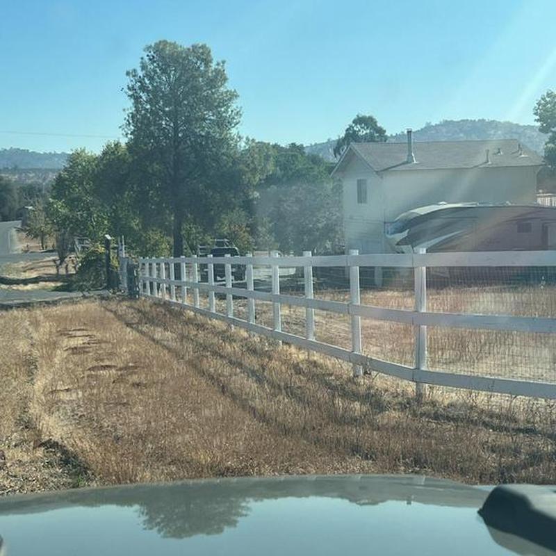 White wooden fence installation along rural driveway